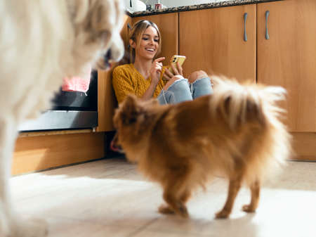 Shot of beautiful young woman using her smart phone while playing with her animals sitting on the...