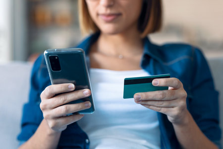 Close-up of beauty young woman holding white credit card for shopping online with mobile phone in living room at home.の写真素材