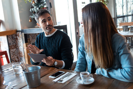 Shot of happy friends group eating burgers while talking about work using digital tablet sitting in restaurant.の写真素材