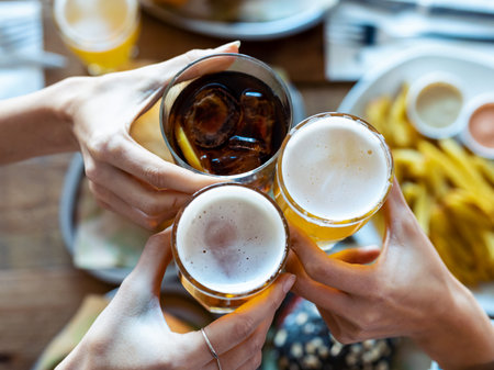 Close up of hand's of young friends toasting with beer while having fun in a restaurant.