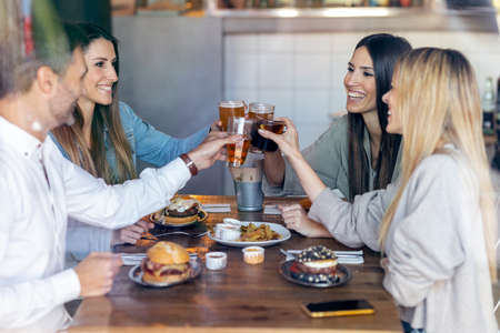 Shot of happy young friends group toasting with beer to celebrating good news while having fun in a restaurant.の写真素材
