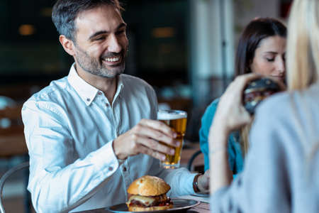 Shot of attractive young friends group eating burgers while talking and having fun in the...
