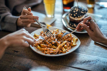 Close-up of hands of friends eating potatoes togheter while having fun in the restaurant.の写真素材