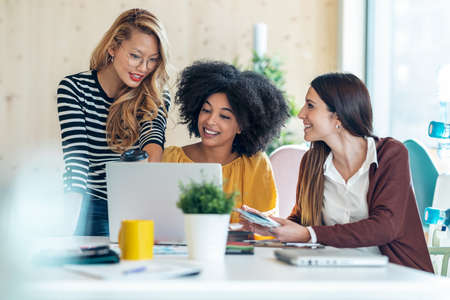 Shot of casual multiethnic business women working with laptops while talking of they new projects together in coworking place.の写真素材