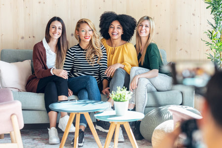 Shot of smiling entrepreneur multiethnic women sitting on couch while taking a picture of them at coworking place.の写真素材