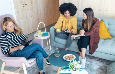 Shot of smart entrepreneur multiethnic women talking while taking a break and showing photos with...