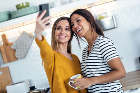 Shot of two beautiful woman friends having breakfast and drinking coffee while talking in the kitchen at home.の写真素材