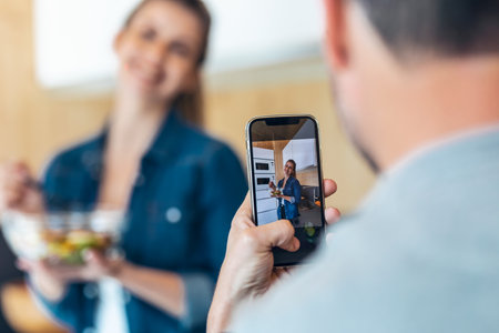 Shot of funny cute couple eating and taking photos with smartphone in the kitchen at home.