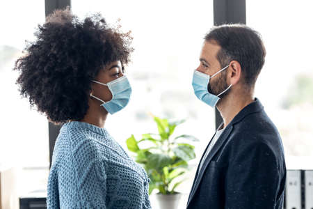 Shot of multiethnic business people with hygienic mask while looking together at eyes in the office.
