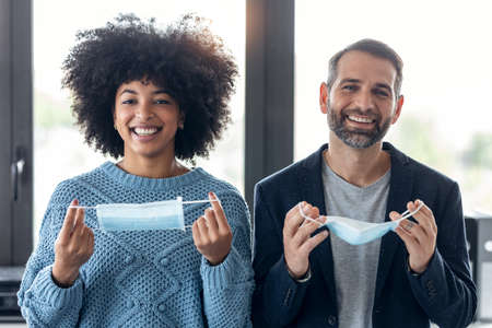 Shot of multiethnic business people taking off an hygienic mask while smiling while looking at camera in the office.の写真素材