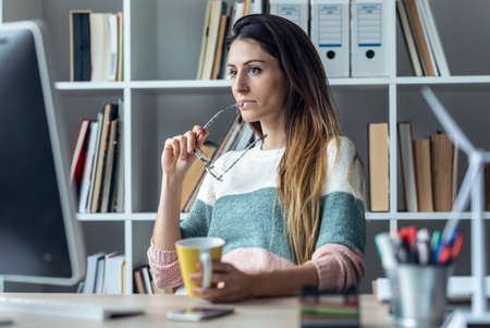 Shot of concentrated young business woman working with computer while drinking coffee in modern...
