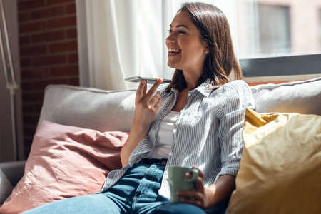 Shot of pretty young smiling woman using mobile phone sitting on a couch at home.
