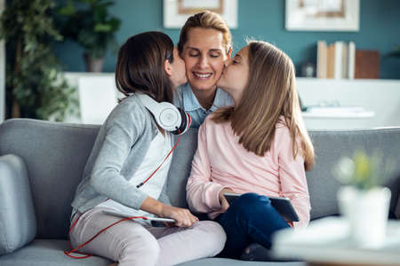 Shot of nice sisters kissing his mother while sitting on couch in the living room at home.
