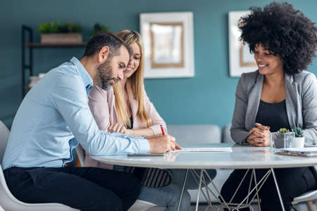 Shot of happy young couple signing bank loan agreement with real-estate agent to buying the house in the office.の写真素材