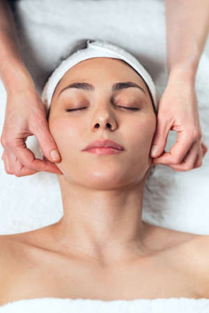 Shot of cosmetologist making face massage for rejuvenation to woman while lying on a stretcher in...