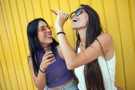 Shoot of two beautiful young women eating ice cream while having fun on yellow background.の写真素材