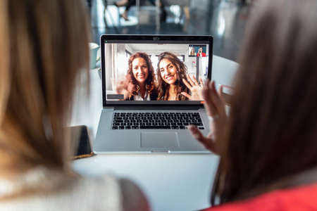 Shot of beautiful women waving hand while doing video call looking at camera in the office at home.の写真素材