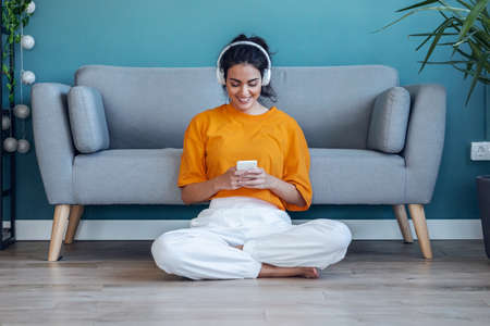 Shot of motivated young woman listening to music with smartphone while dancing sitting on the floor at home.の写真素材