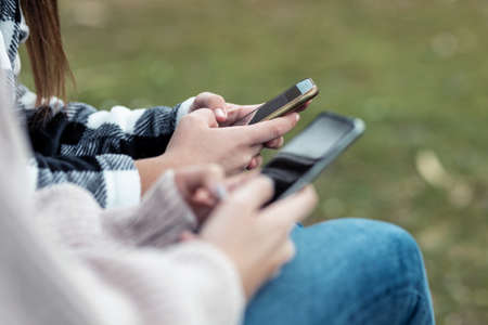 Close-up of two girls using and chatting with their smartphones ar the park.の写真素材