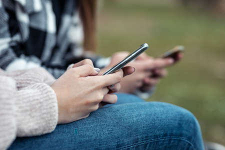 Close-up of two girls using and chatting with their smartphones ar the park.の写真素材
