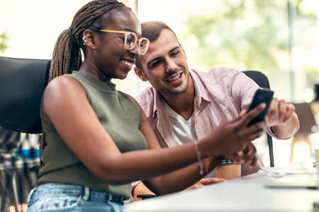 Shot of happines business team taking a break of work while looking photos in smartphone in a coworking place.の写真素材