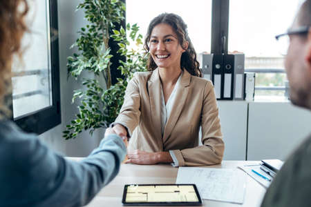 Shot of attractive real-estate agent shaking hands with young couple after signing agreement contract in a real estateの写真素材