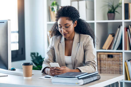 Shot of elegant business woman sending messages with mobile phone while working in the office.