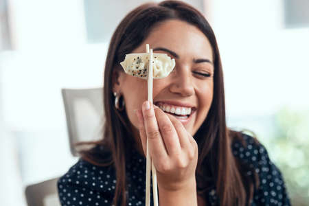 Shot of funny business woman holding gyoza with chopsticks while having lunch in the office