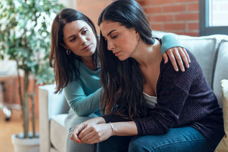 Shot of pretty young woman supporting and comforting her sad friend while sitting on the sofa at home.の写真素材