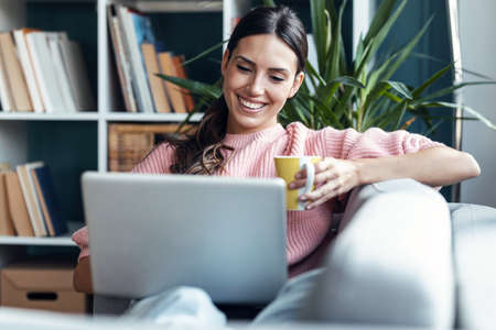 Shot of cute woman having videocall with friends on laptop sitting on the couch at home.