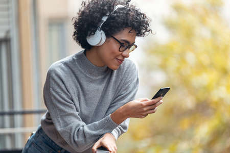 Shot of beautiful woman using her smartphone while listening to music standing in the balcony at home.の写真素材