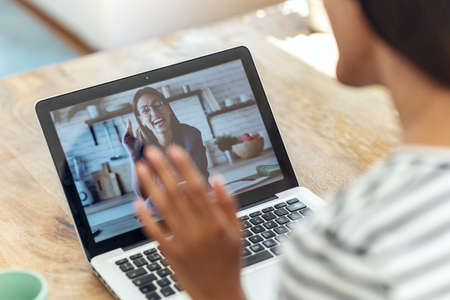 Back view of business woman speaking on video call with a friend with laptop while sitting on living...