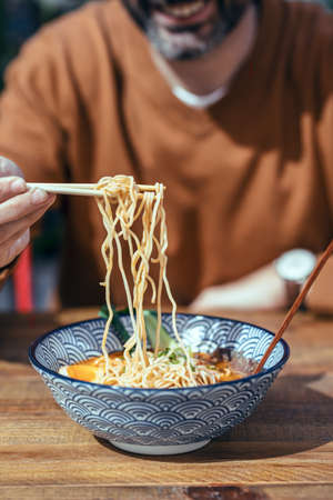 Close up of handsome mature man eating ramen with chopsticks in an asian restaurantの写真素材