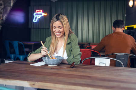 Shot of funny beautiful woman eating ramen with chopsticks in asian restaurant.の写真素材