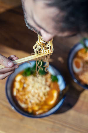 Close up of handsome mature man eating ramen with chopsticks in an asian restaurantの写真素材