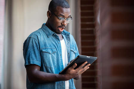 Shot of surprised businessman working with digital tablet while standing near windows in a coworking...
