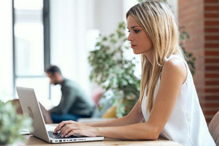 Shot of beautiful young woman using computer while her husband relaxing sitting on the couch at home.の写真素材
