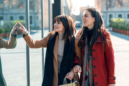 Shot of two beautiful friends talking and having fun while walking on the city street with shopping bag.の写真素材