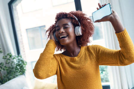 Shot of beautiful woman listening to music with headphones while dancing in the living room at home.