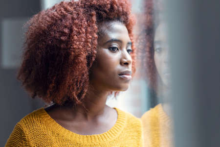 Portrait of concentrated young woman looking forwards at window while standing in the living room at home.の写真素材