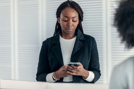 Shot of beautiful woman using her mobile phone while listening to her partner in a modern startup.の写真素材