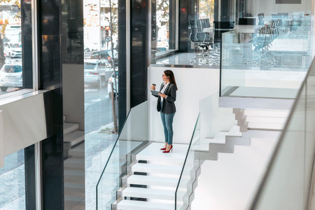 Shot of businesswoman working with a digital tablet while drinking coffee going down the office stairs.の写真素材