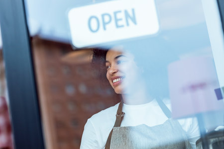 Portrait of beautiful young woman hanging the open sign on a glass door in the pastry shop.