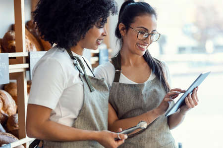 Shot of couple women owners bakery working while analyzing report for order delivery with digital tablet in a pastry shop.の写真素材
