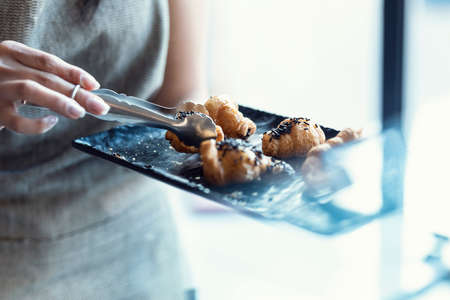 Close up of hands of the pastry woman grabbing a tray of chocolate croissants to serve a customer in the pastry shop.の写真素材