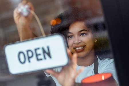 Portrait of beautiful young woman hanging the open sign on a glass door in the pastry shop.