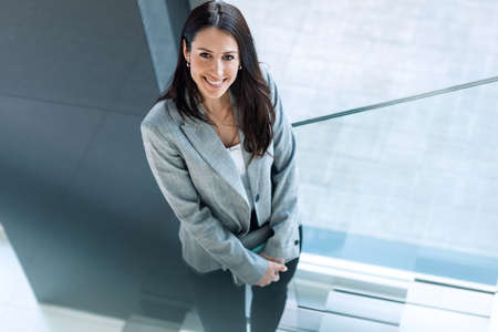 Shot of beautiful business woman holding digital tablet while looking at camera standing on stairs...