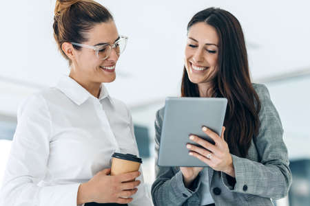 Shot of two attractive young business women working with digital tablet while talking and walking in a modern startup.の写真素材