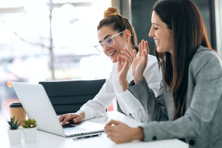 Shot of beautiful women waving hand while doing video call looking at camera in the office at home.