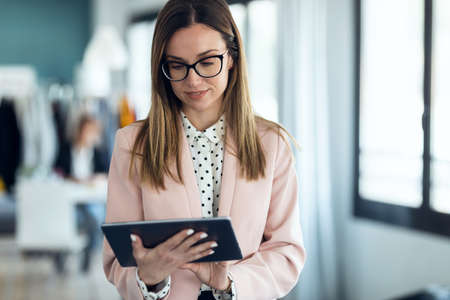 Portrait of smart young businesswoman looking at camera while holding her digital tablet on coworking place.の写真素材